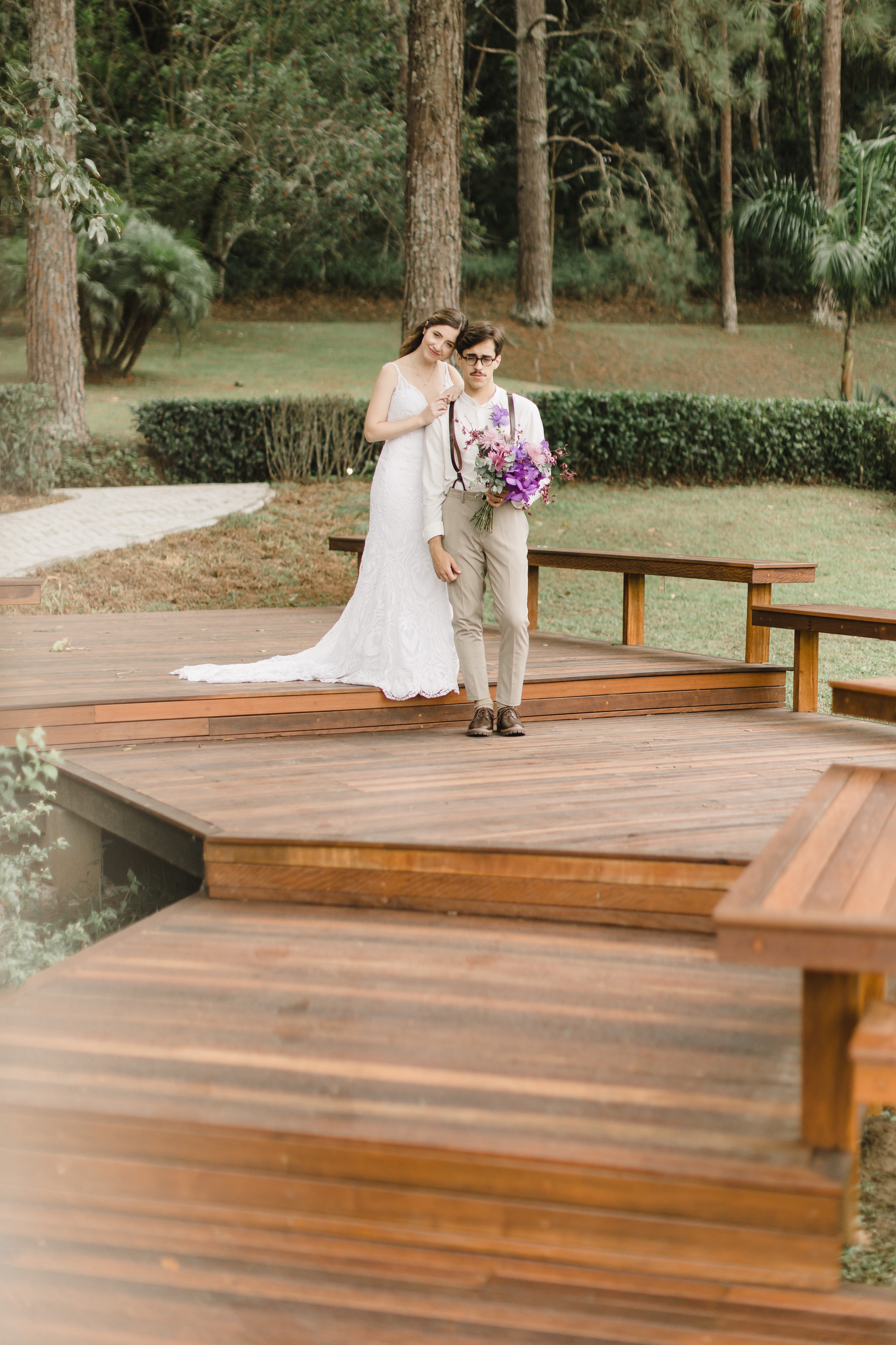 Casal de noivos posando no deck de madeira com jardim ao fundo