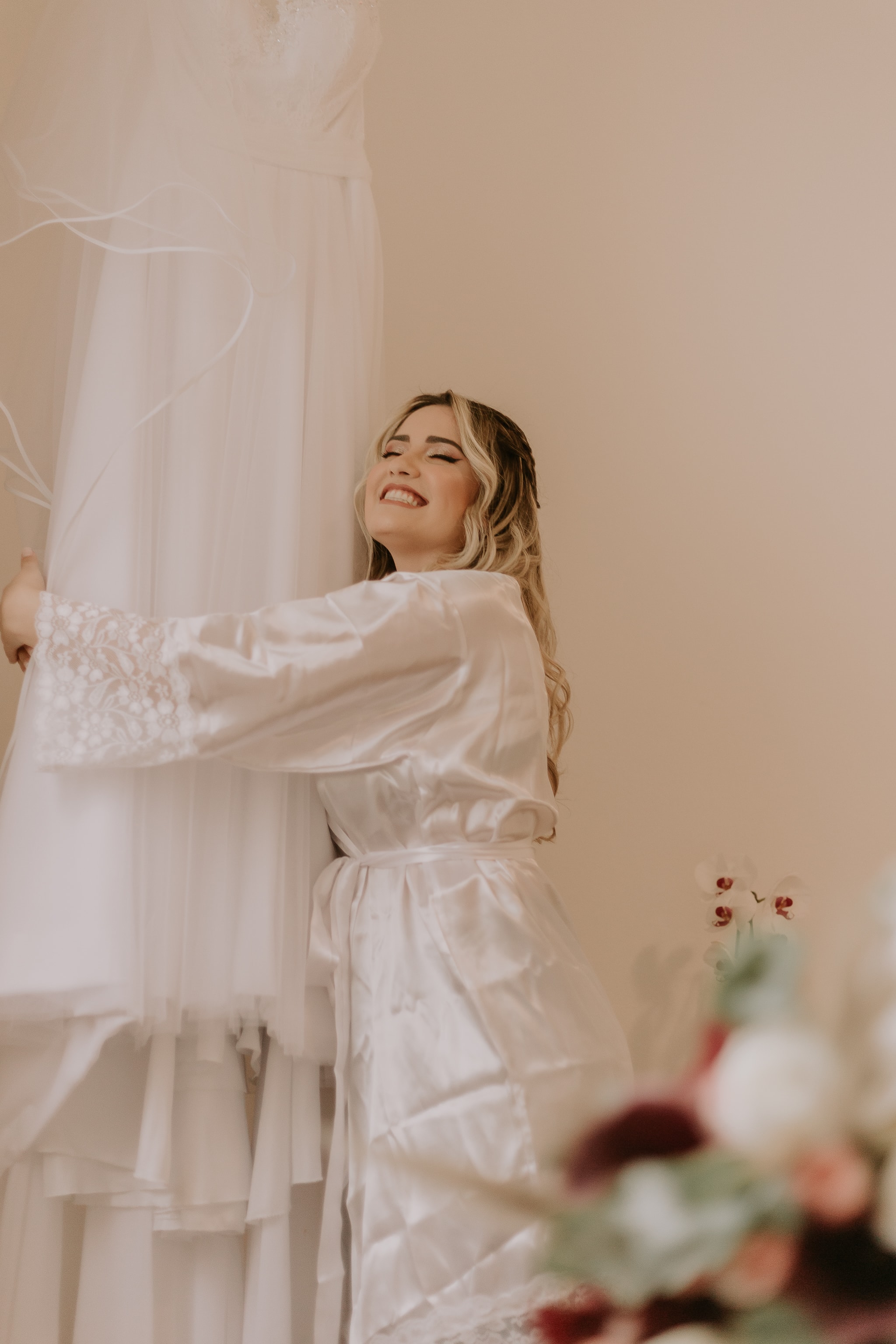 Noiva sorrindo abraçando o vestido de noiva antes da cerimônia