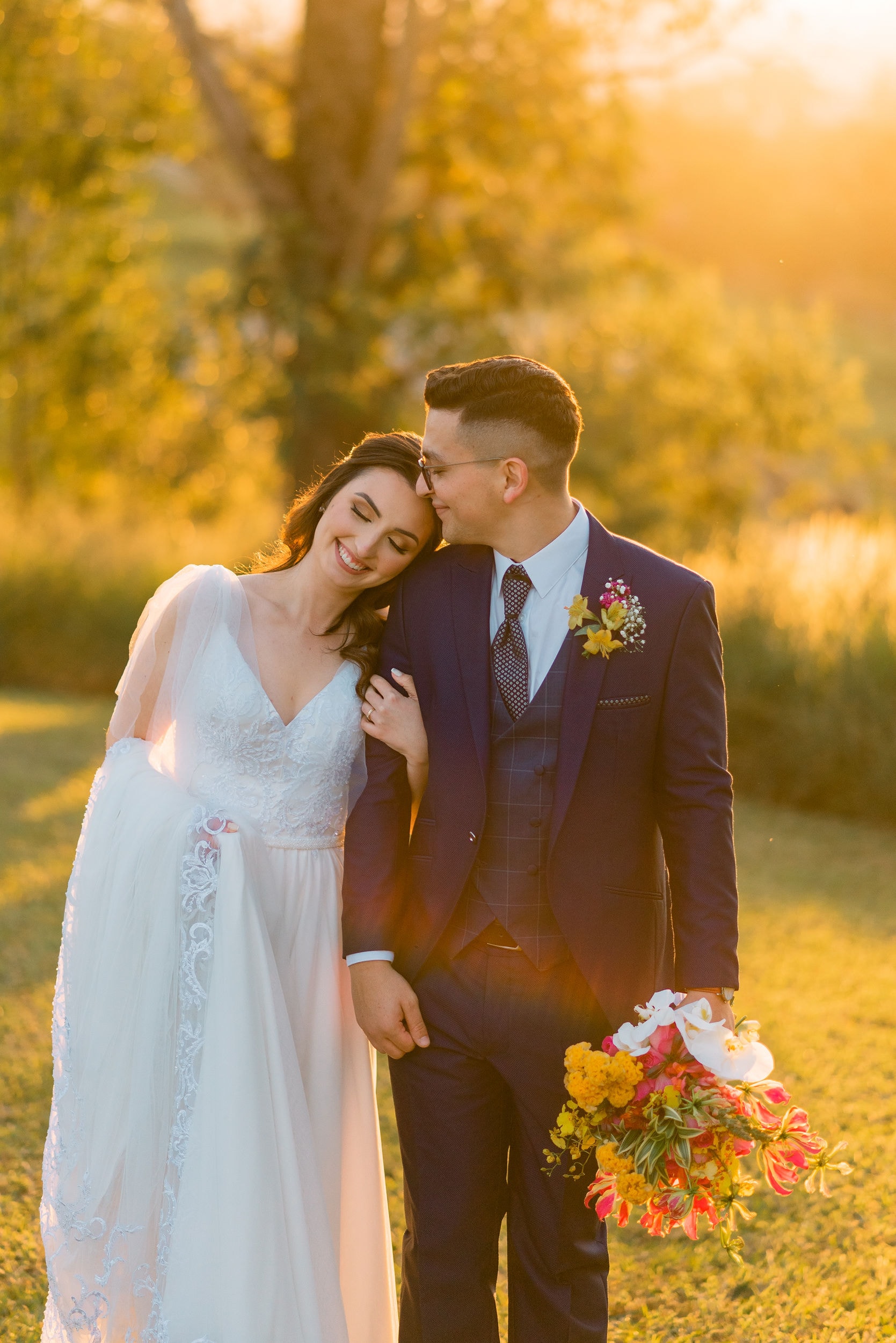 Casal de noivos ao pôr do sol dourado com buquê colorido