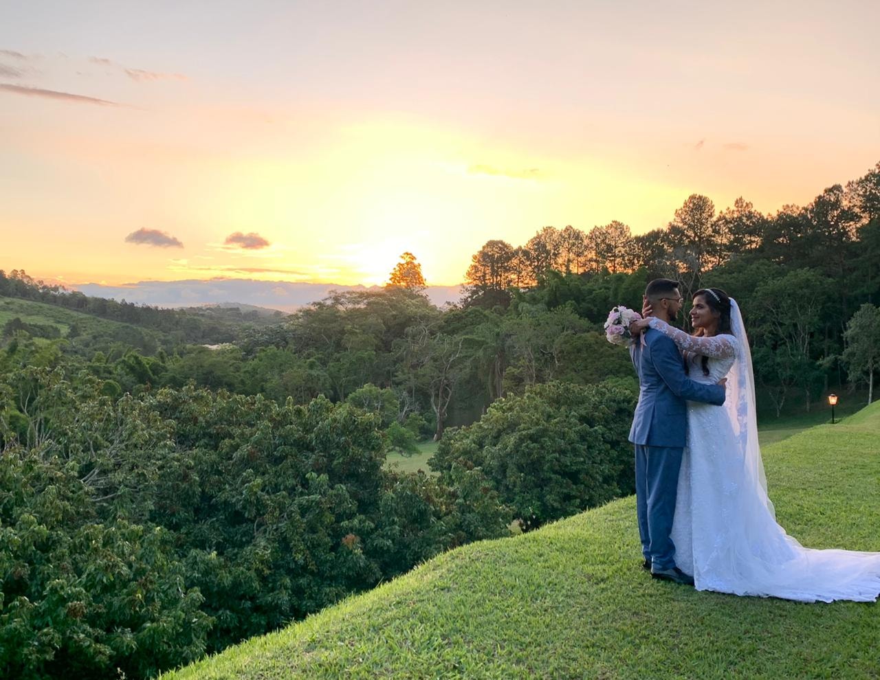 Casal de noivos abraçados no topo da colina com vista panorâmica da Mata Nativa ao pôr do sol