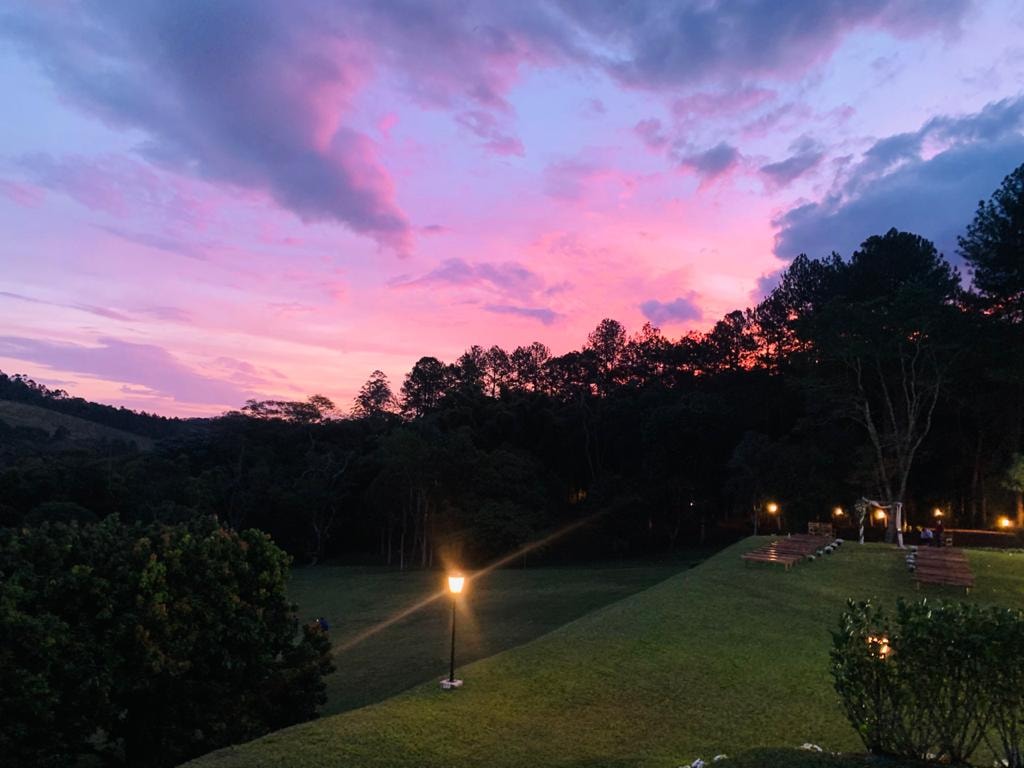 Pôr do sol rosa e roxo sobre o gramado do Eco Espaço com lanternas iluminadas