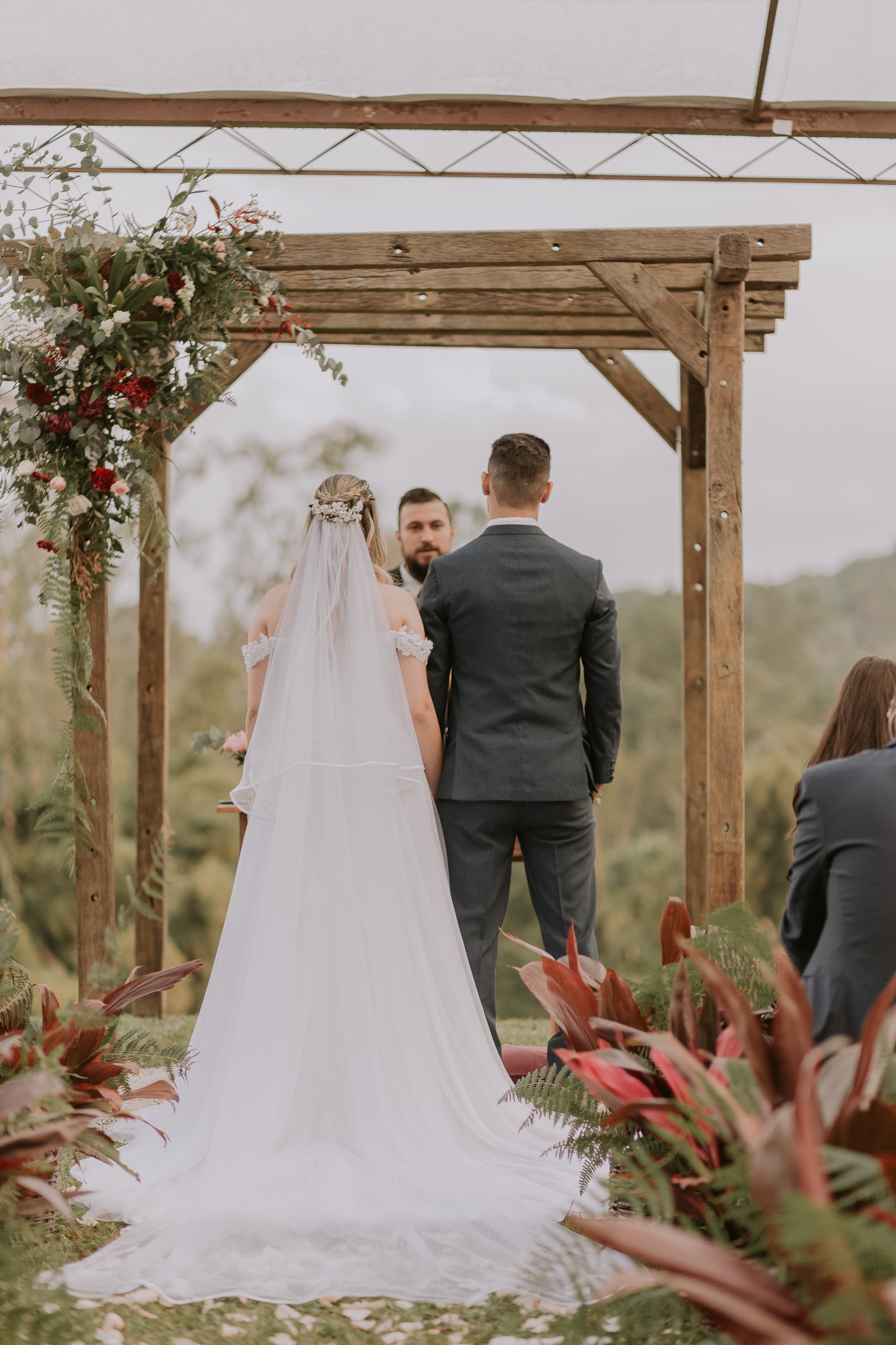 Casal de costas durante cerimônia ao ar livre sob pérgola de madeira com flores