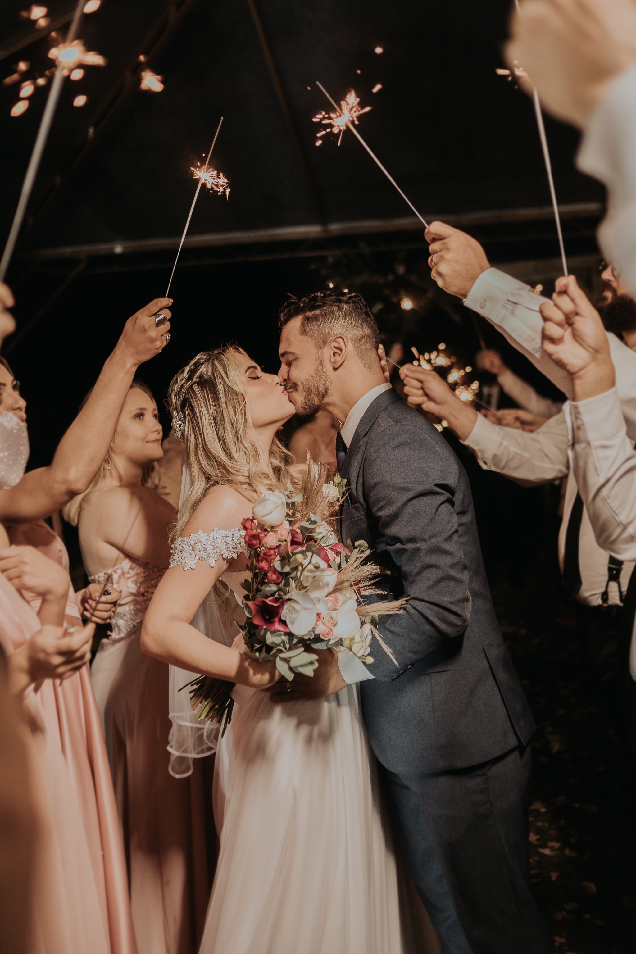 Casal se beijando rodeado de convidados com sparklers durante saída da festa