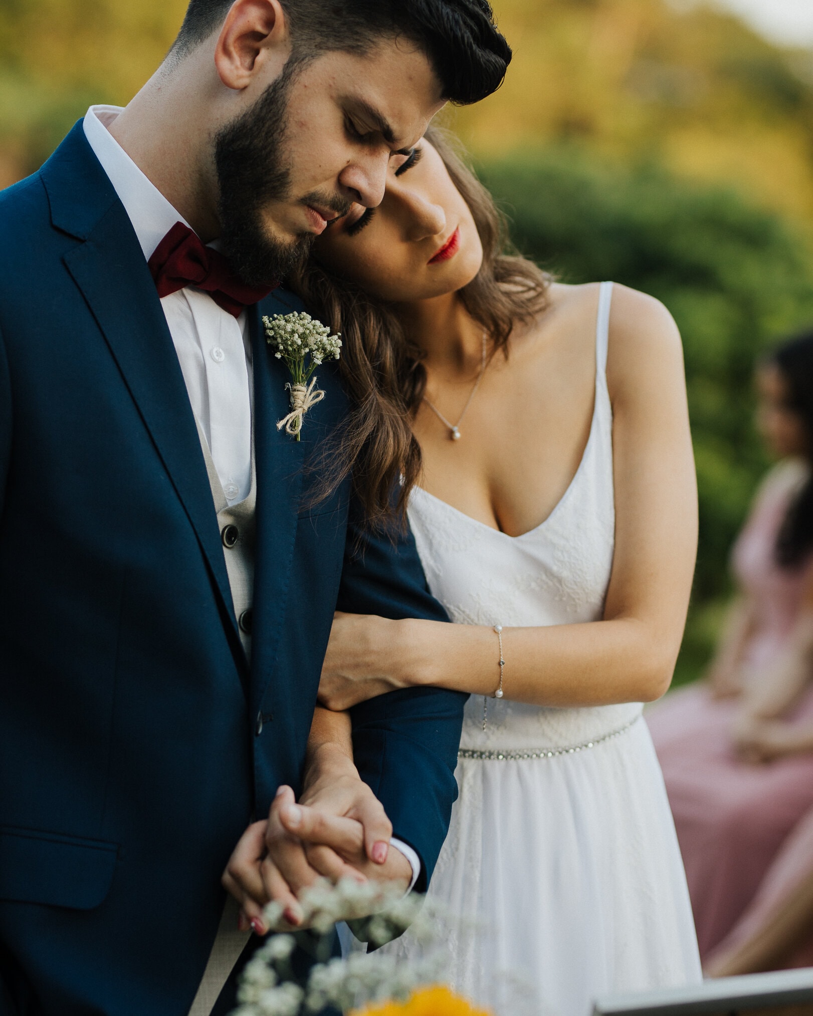 Casal de noivos de mãos dadas durante cerimônia ao ar livre com flores ao fundo