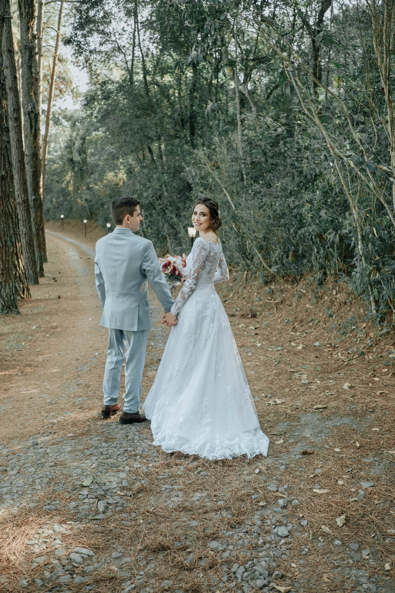 Noiva sorrindo de costas com vestido de renda em caminho de pedras na floresta