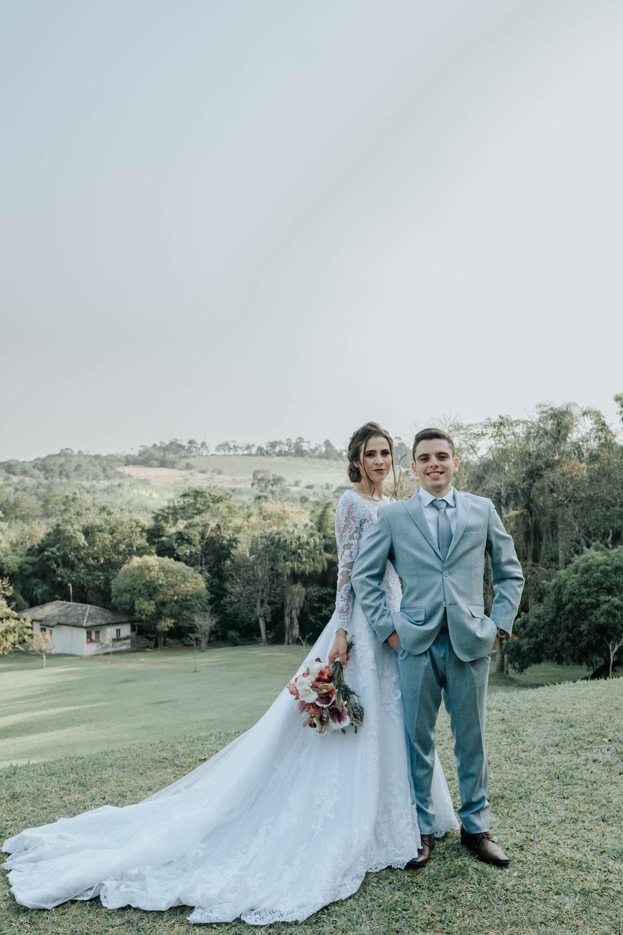 Casal de noivos posando no gramado com vista panorâmica das colinas do Eco Espaço