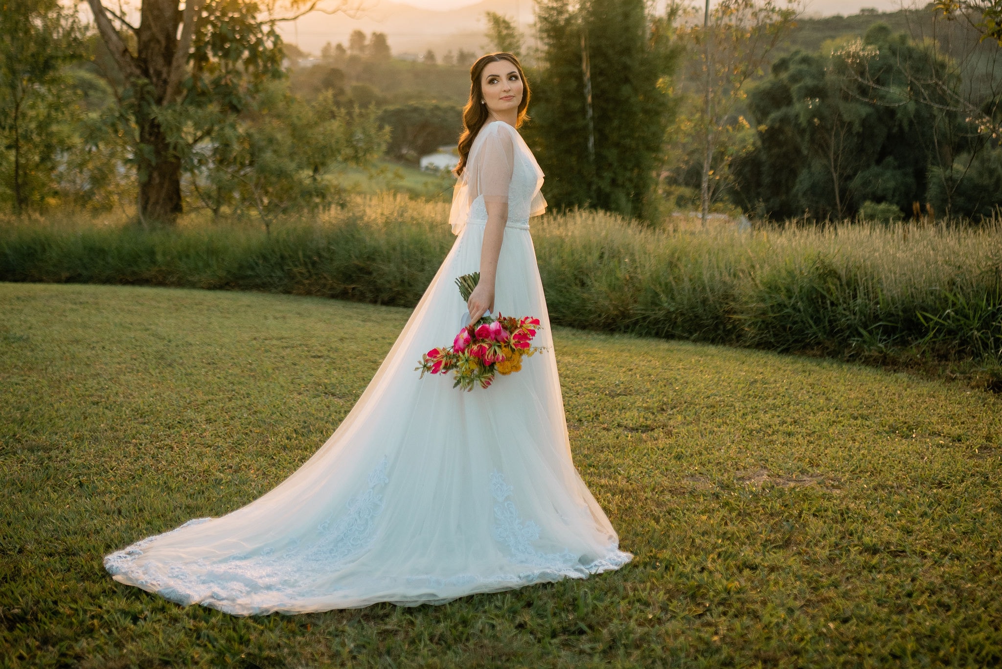 Noiva com vestido de cauda longa no jardim ao pôr do sol