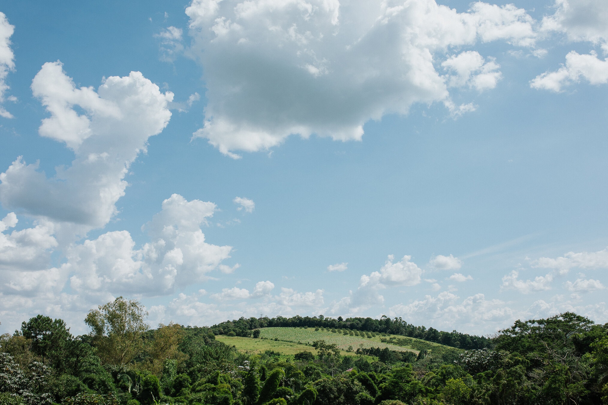 Vista das colinas verdes do Eco Espaço sob céu azul com nuvens brancas
