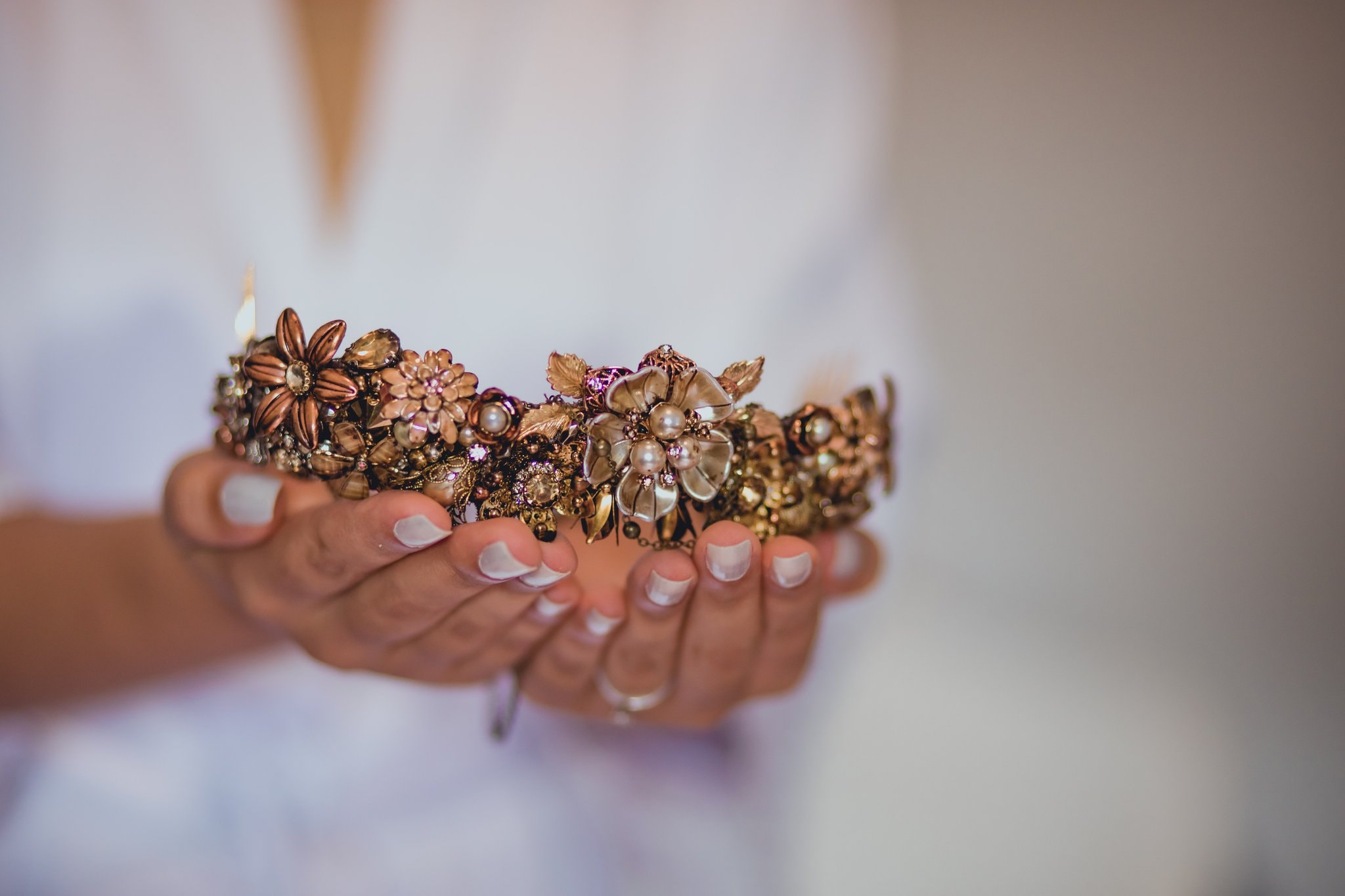 Noiva segurando tiara floral dourada com pérolas e detalhes artesanais