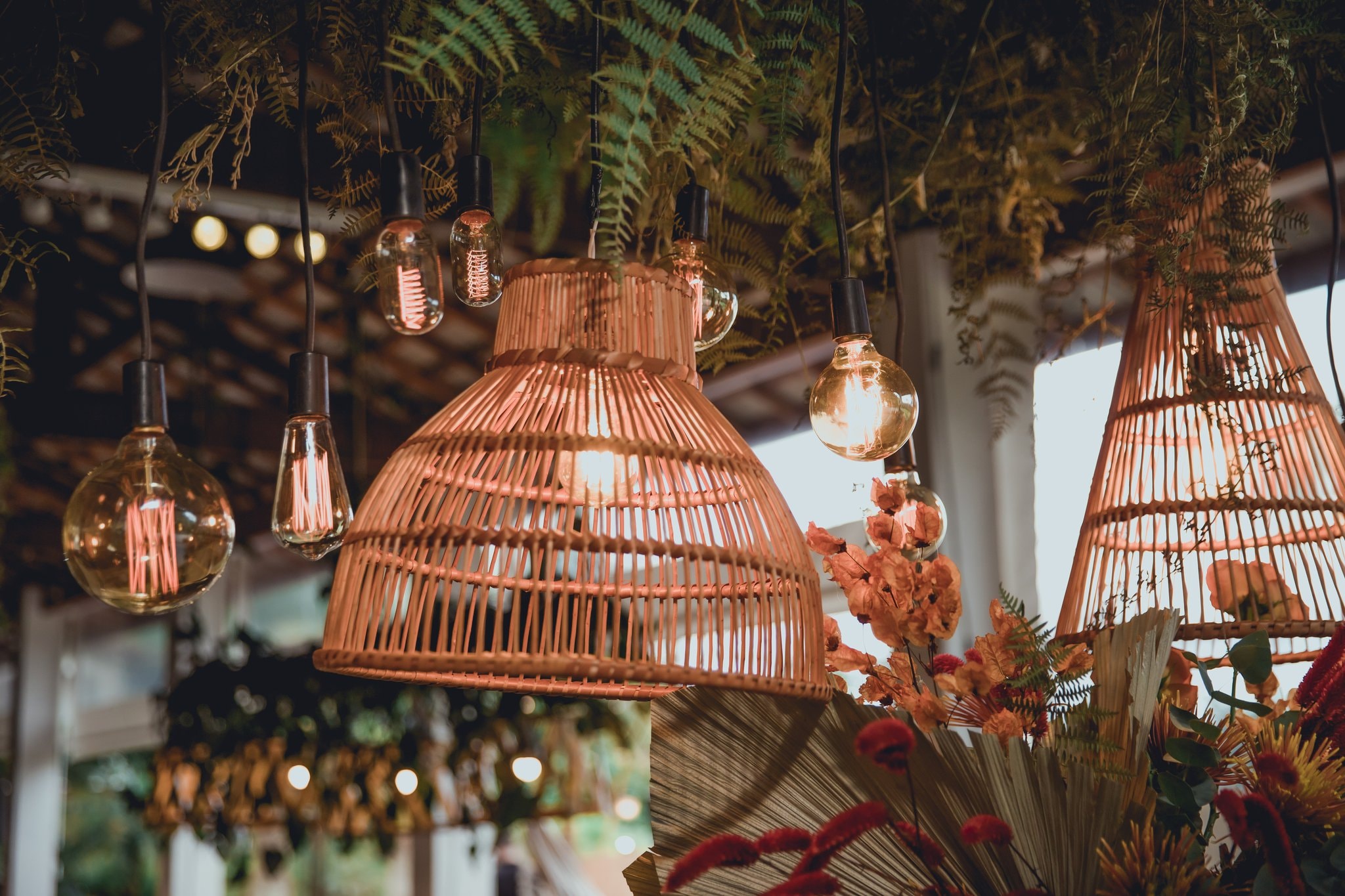 Luminárias de vime e lâmpadas Edison suspensas com samambaias e flores secas na decoração do salão