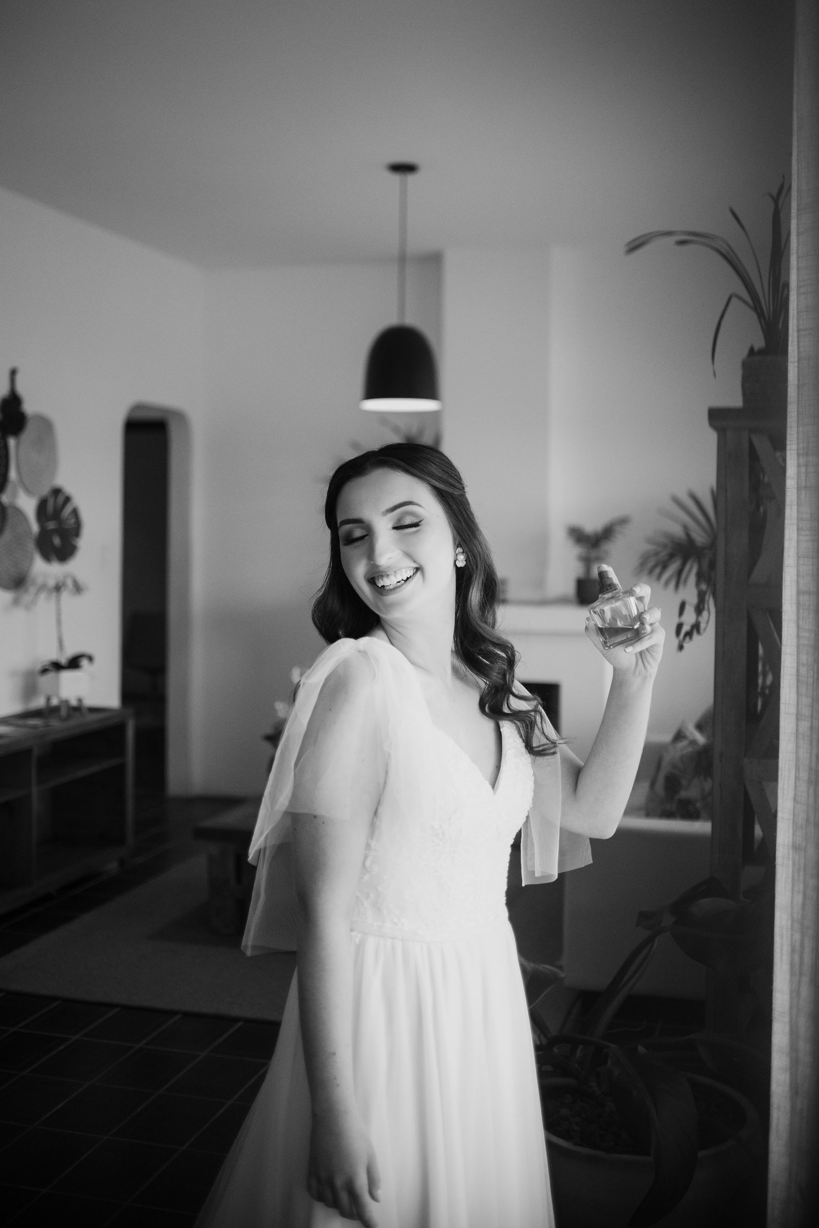 Noiva em preto e branco sorrindo com perfume na mão
