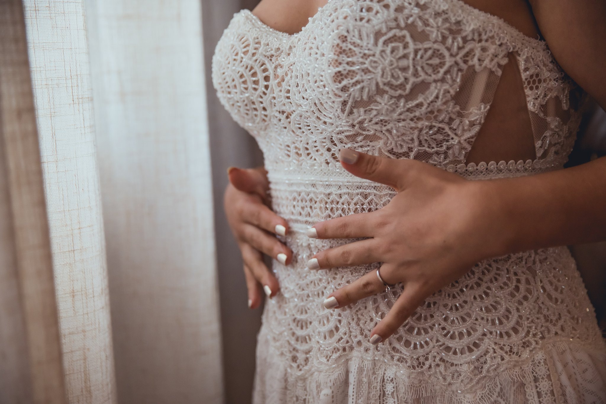 Detalhe do vestido de noiva em renda com mãos ajustando o corpete durante o making of